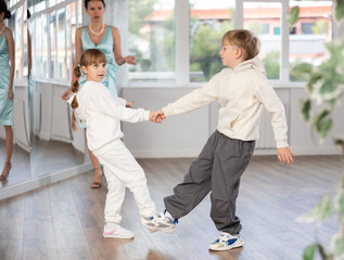 Boy and girl kids repeat movement while taking boogie woogie dancing lessons. Female teacher...