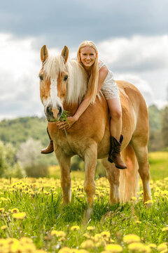 Young woman riding her Haflinger horse bareback in a blooming meadow on a sunny spring day