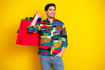 Young man with a colorful shirt carries shopping bags against a bright yellow background for summer...