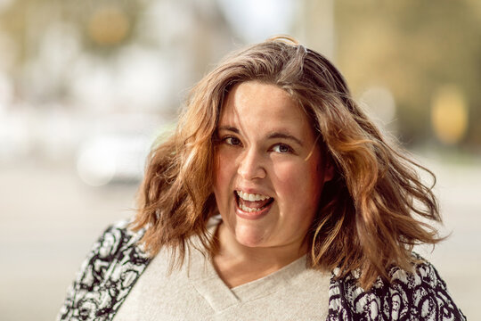 Cheerful woman with wavy brown hair smiling outdoors in natural light and casual outfit