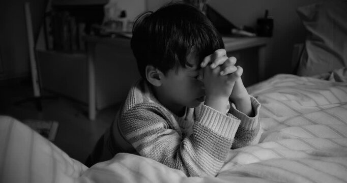 Boy kneeling at bedside with eyes closed and hands clasped in prayer, symbolizing childhood innocence, faith, devotion, and search for comfort and hope in adversity