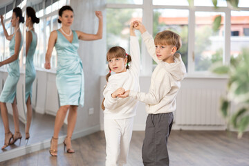 Boy and girl kids in sport wear repeat movement while taking rumba dancing lessons. Female teacher...