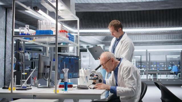 Senior chemist and coworker observing specimen under microscope in the laboratory. Clinical experiment illustrates discovery process in bioscience and molecular research for innovation.