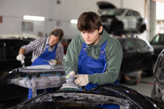 Male mechanic prepares car for painting in workshop - using grinding machine he sands the bumper before painting - Powered by Adobe