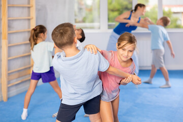 Naklejka premium Preteen children practicing in pair self-defence movements with female trainer supervision