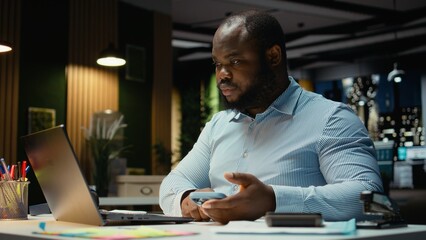 Overworked male worker checking calendar before scheduling engagement, picking up his smartphone to...