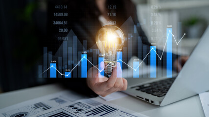 Business professional holding light bulb symbolizes innovation while analyzing financial data...