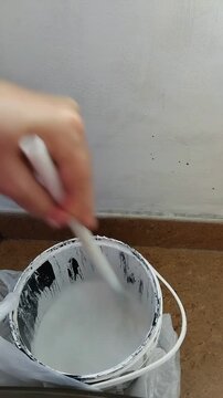 Una mano de mujer moviendo un palo en una pintura de color blanco para pintar la pared su casa. Video vertical