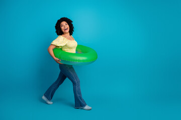 Charming young woman holding bright green inflatable ring, cheerful on vibrant turquoise background, summer vibes