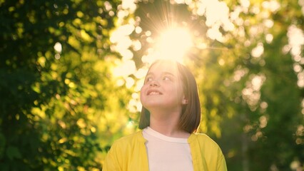 Child dreams in nature. Happy little girl smiles in sun park. Girl smile in forest, face child close-up. Happy portrait of teenager in sun. Family in nature. Beautiful face. Freedom of childhood, life