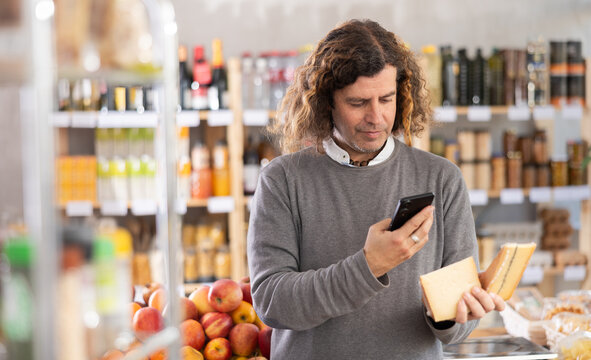 Adult man scans a barcode of a cheese package on his mobile. Buyer scans the QR code on his phone to pay at the supermarket checkout - Powered by Adobe