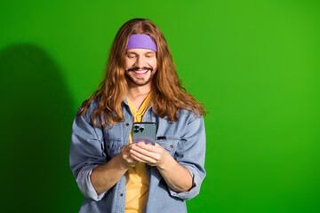 Young boho style man using a smartphone with a green screen background, smiling and showcasing technology in casual fashion