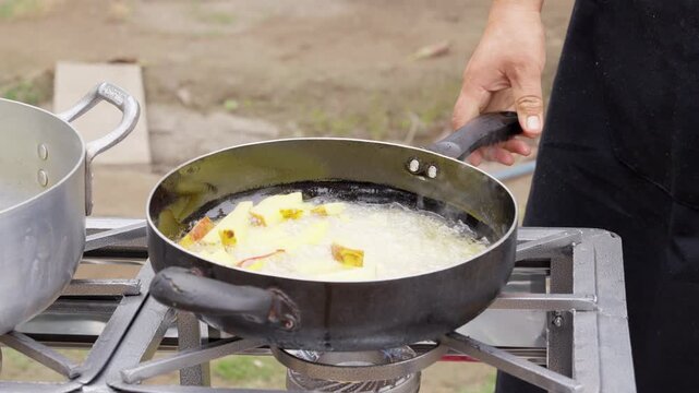 Chef deep frying potatoes in hot oil outdoors at country restaurant
