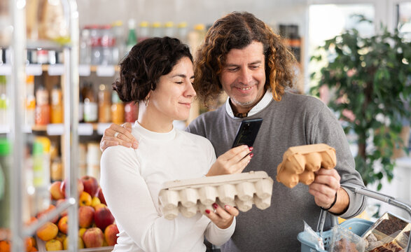 Checking expiration date of eggs - wife and husband shoppers scans QR code on label of eggs using her smartphone - Powered by Adobe