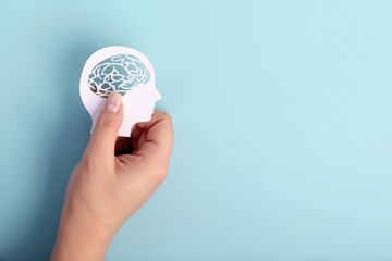 Hand holding a paper cutout human head silhouette with a brain, representing mental health, psychology, and thoughts