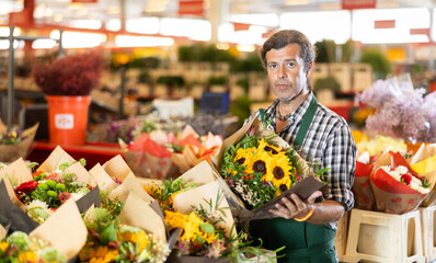 Ьale consultant seller holds bouquet of cut flowers in hands, gets acquainted with assortment, checks goods before sending them to customer.