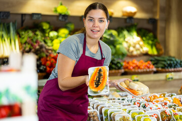 Female grocery store worker offers various packaged fruits and vegetables