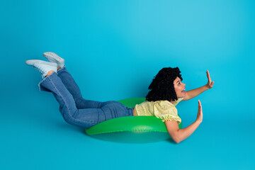 Young woman in casual attire joyfully posing with inflatable green prop on a vibrant blue backdrop,...
