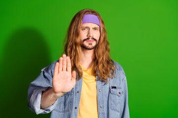 Young man making hand stop gesture in front of vibrant green background showcasing casual hippie...