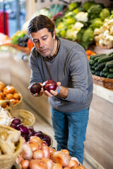 Adult man chooses onions for purchase in greengrocer shop
