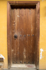A weathered wooden doorway with iron studs and a small metal ring, photographed in soft daylight. Rustic wall texture from Turkey Bursa for travel guides, real estate, hospitality, heritage branding.