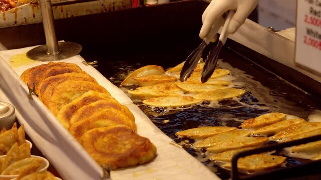 Vendor frying golden Korean mandu dumplings on a hot griddle at a bustling Seoul street food stall