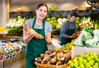 Young woman in apron sells cassava in vegetable shop