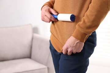 Fototapeta premium Man cleaning sweater with lint roller at home, closeup. Space for text