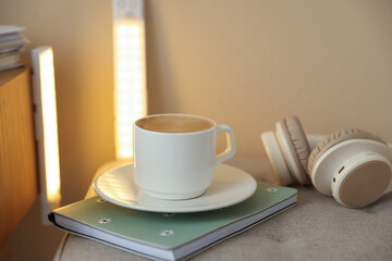 Coffee, notebook, headphones on pouf and portable LED lamps at home, closeup