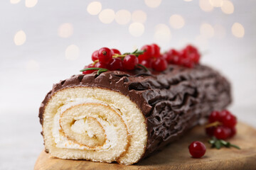 Delicious Yule log (traditional Christmas cake) with redcurrant on table against blurred lights, closeup. Bokeh effect