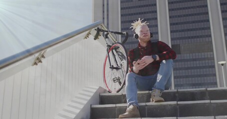 Holding smartphone, man wearing shirt, headphones sitting on urban steps by red bike, copy space