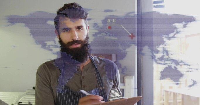 Writing bearded kitchen manager jotting notes on clipboard at restaurant kitchen, with world map