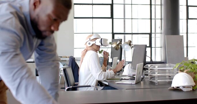 Navigating South Asian woman in hijab and VR headset exploring interface at office, with monitors - Powered by Adobe