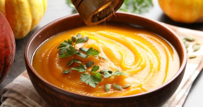 Woman salting tasty pumpkin cream soup in bowl at table, closeup