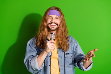 Cheerful young man with long hair holding a microphone against a vibrant green backdrop in retro...