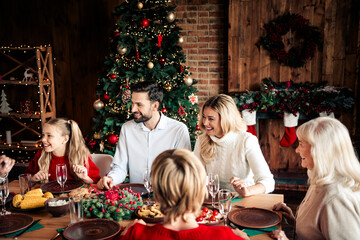 Family Christmas dinner around a warm festive table beside a decorated Christmas tree and cozy...