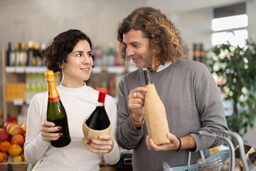 Husband and wife choose a quality Spanish wine for a romantic dinner. Shoppers in a supermarket hold bottles of wine and champagne in their hands, looking at the price and manufacturer