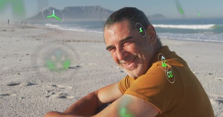 Senior man sitting on beach turning head smiling at camera eco icons swirling for sustainability - Powered by Adobe