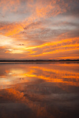 Fototapeta premium Sunset over the salt lakes in Spain with vivid orange and golden reflections on calm water under dramatic clouds.