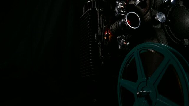 An 8mm vintage film projector operating. Film reel turning and light through lens. Classic home movie theater projection lens.