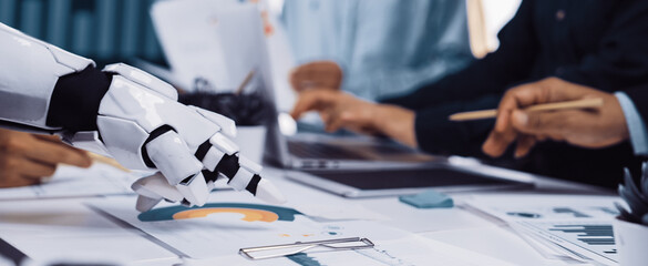 A robotic arm collaborates with human hands in a modern office, analyzing business data and documents, showcasing the integration of technology in the workspace.Noogenesis