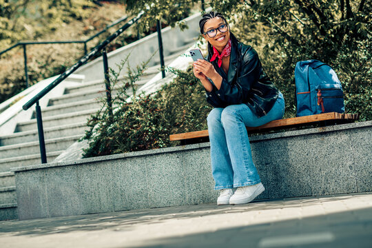 Lovely woman enjoying outdoor leisure activities while using her smartphone on a sunny day in an urban park setting. - Powered by Adobe