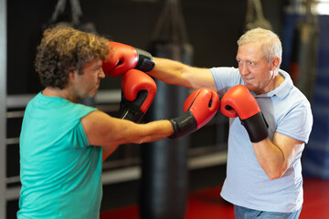 Determined older trainee mastering self-defense techniques, practicing punches in sparring with...