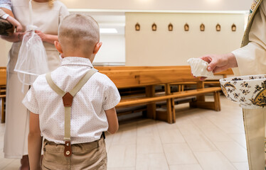 Child at Baptism Ceremony in Church – Boy Standing Before Priest Holding Holy Water Shell and...
