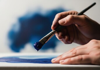 Painter hand with brush applying vibrant blue paint to a white canvas, artistic process