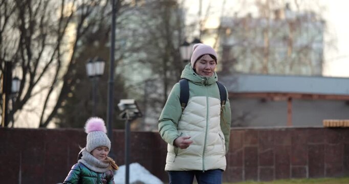 Mother in green puffer jacket walking with child in winter park, enjoying outdoor activity, surrounded by grass and snow, showcasing family bonding and playful moments in a serene environment