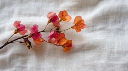 A single branch of pink and orange flowers with green leaves on a white fabric background.
