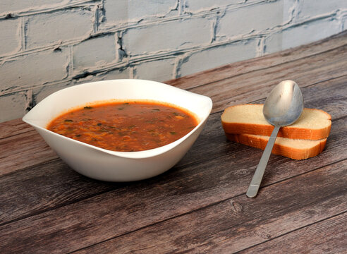 Caucasian soup Kharcho with spices in a deep ceramic plate on a wooden table, next to it a tablespoon and two pieces of bread.