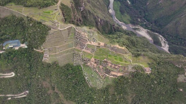 A dynamic drone shot circles with a downward-facing angle while simultaneously flying upwards, creating a spiraling reveal of Machu Picchu's entire size and its vast surrounding mountain landscape