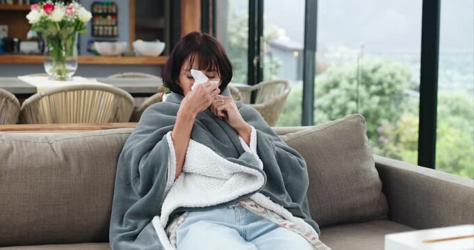 Cold, sick and woman with blanket on couch from allergies, flu symptoms and blowing nose of virus. Mature person, tissue or sinus with nasal congestion, viral infection and influenza recovery in home